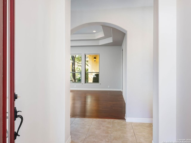 hall featuring crown molding, light hardwood / wood-style flooring, and a tray ceiling