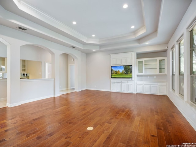 unfurnished living room with hardwood / wood-style floors, crown molding, and a tray ceiling