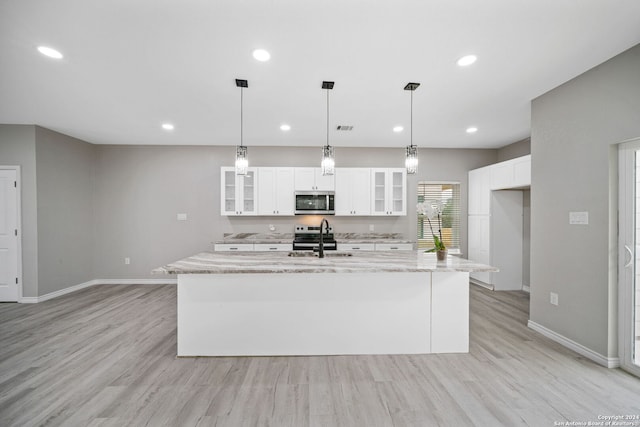 kitchen with white cabinets, an island with sink, light stone countertops, light hardwood / wood-style flooring, and stainless steel appliances