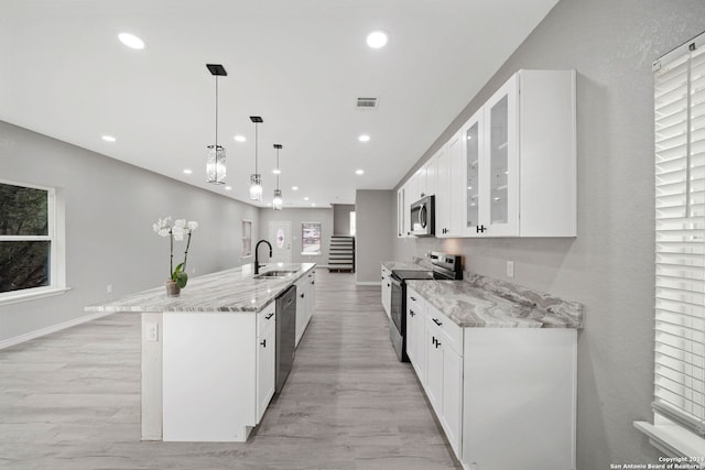 kitchen featuring light wood-type flooring, an island with sink, hanging light fixtures, stainless steel appliances, and white cabinets