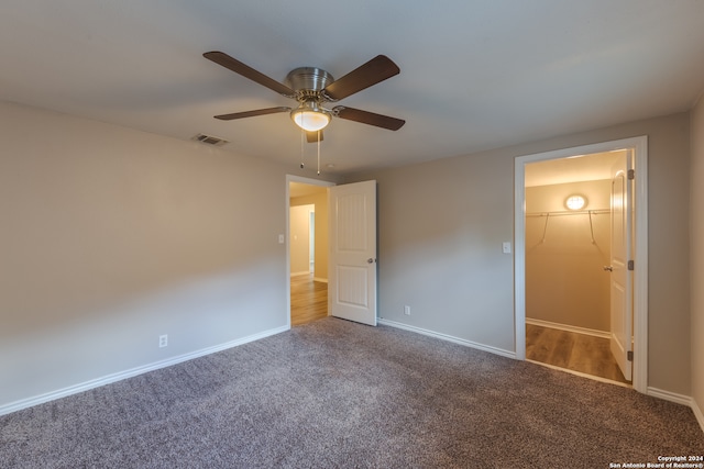 unfurnished bedroom with a closet, a spacious closet, carpet flooring, and ceiling fan