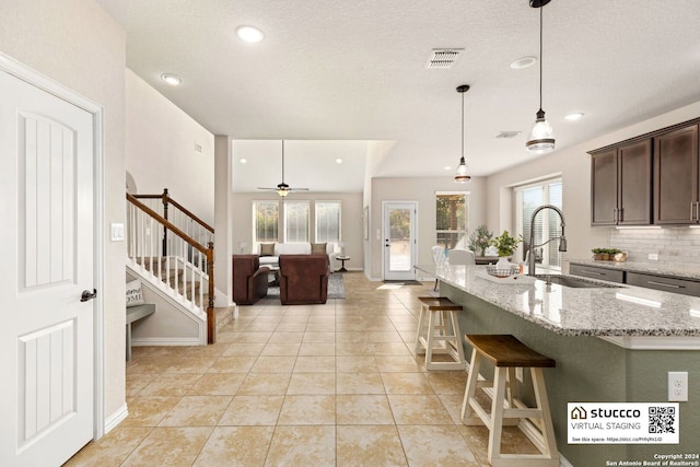 kitchen with hanging light fixtures, light stone counters, ceiling fan, dark brown cabinetry, and sink