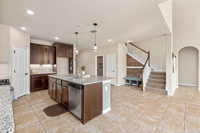 kitchen featuring light stone countertops, sink, hanging light fixtures, stainless steel appliances, and a center island with sink