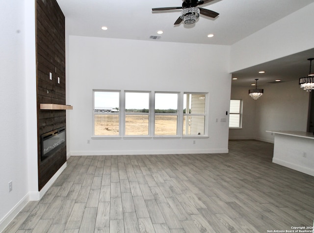 unfurnished living room with light hardwood / wood-style flooring, a large fireplace, and ceiling fan with notable chandelier