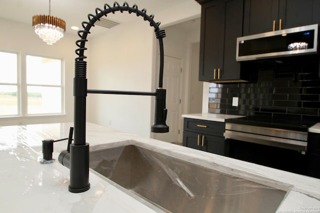 kitchen with appliances with stainless steel finishes, decorative light fixtures, tasteful backsplash, light stone counters, and an inviting chandelier