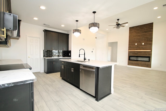 kitchen with an island with sink, sink, a large fireplace, hanging light fixtures, and stainless steel dishwasher