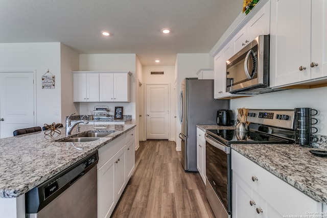 kitchen with appliances with stainless steel finishes, sink, light wood-type flooring, white cabinets, and light stone counters