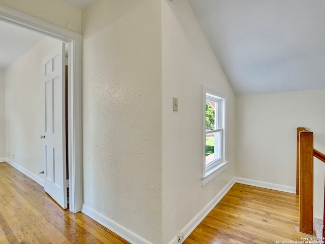 corridor with light hardwood / wood-style floors and lofted ceiling