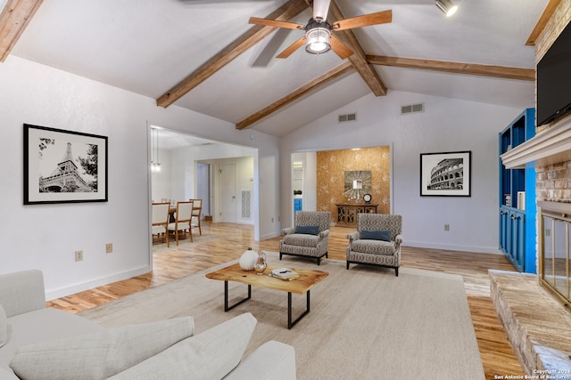 living room with a brick fireplace, light wood-type flooring, vaulted ceiling with beams, and ceiling fan