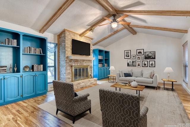 living room with ceiling fan, a textured ceiling, vaulted ceiling with beams, a brick fireplace, and light wood-type flooring