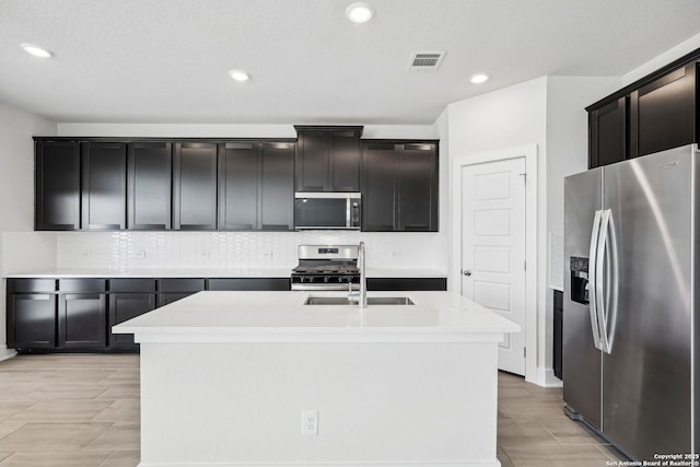 kitchen with sink, decorative backsplash, an island with sink, and appliances with stainless steel finishes