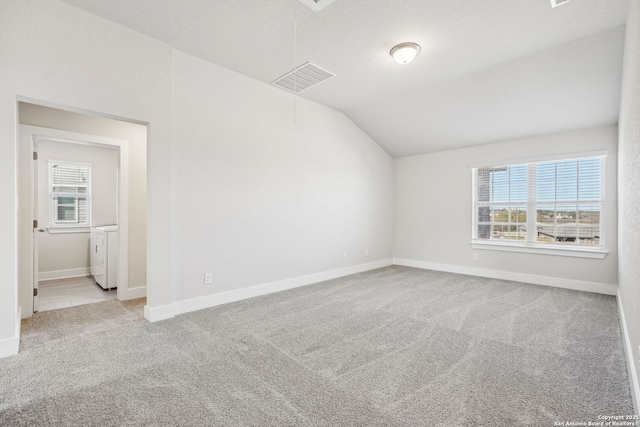 empty room with light carpet, washing machine and clothes dryer, vaulted ceiling, and a textured ceiling