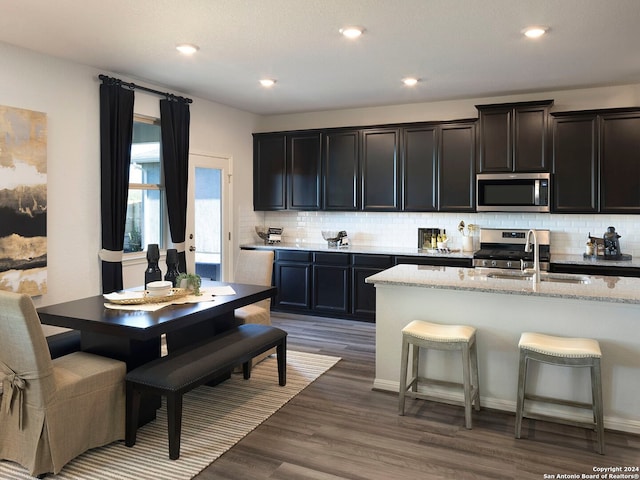 kitchen featuring sink, stainless steel appliances, an island with sink, dark hardwood / wood-style flooring, and decorative backsplash