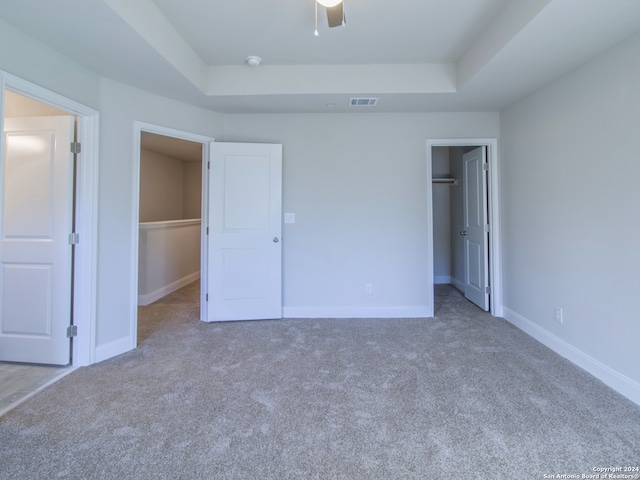 unfurnished bedroom featuring light carpet, ceiling fan, a raised ceiling, a closet, and a walk in closet