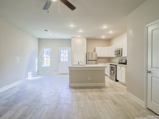 kitchen with white cabinetry, stainless steel appliances, light hardwood / wood-style flooring, and a center island with sink