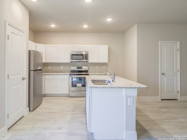 kitchen featuring sink, light wood-type flooring, white cabinetry, appliances with stainless steel finishes, and light stone counters