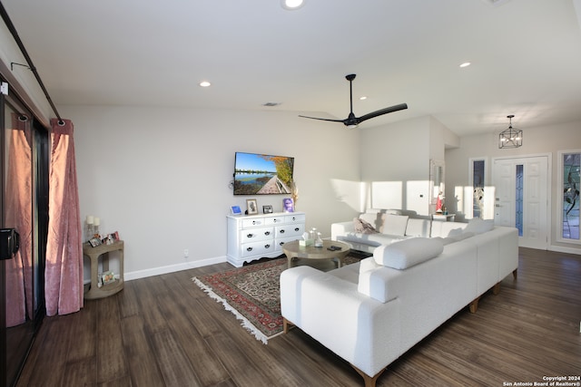 living room featuring dark wood-type flooring, ceiling fan with notable chandelier, and vaulted ceiling