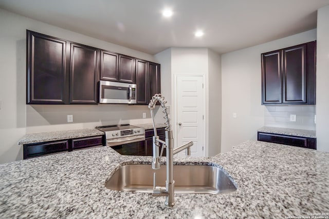 kitchen with light stone countertops, appliances with stainless steel finishes, dark brown cabinets, and sink