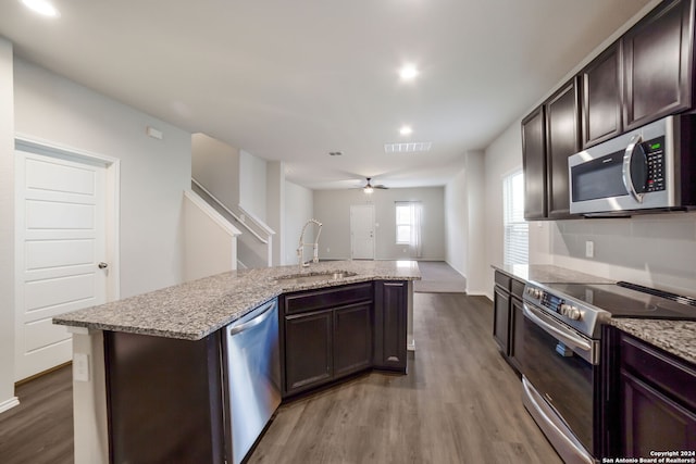 kitchen featuring appliances with stainless steel finishes, dark brown cabinets, a kitchen island with sink, sink, and hardwood / wood-style flooring