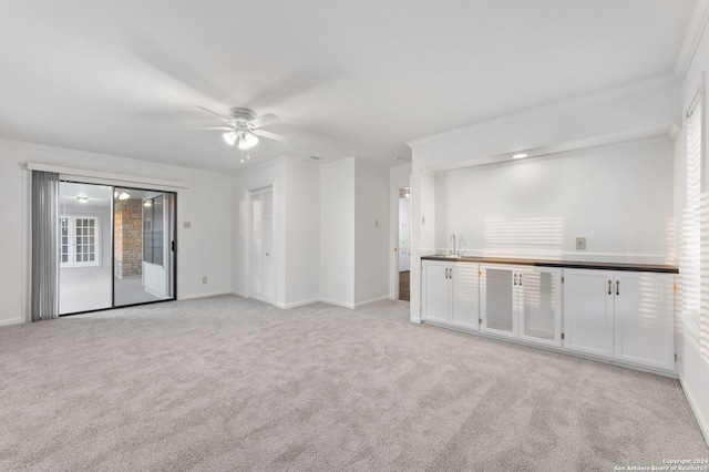 unfurnished living room featuring crown molding, sink, light colored carpet, and ceiling fan