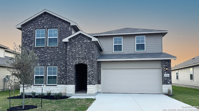 traditional-style house with concrete driveway, a garage, brick siding, stone siding, and a lawn