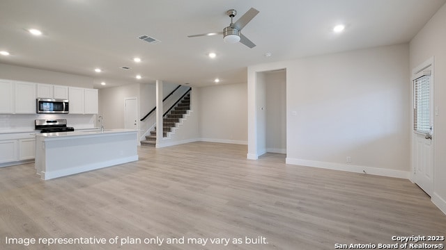 kitchen featuring a kitchen island with sink, stainless steel appliances, white cabinets, light hardwood / wood-style floors, and ceiling fan