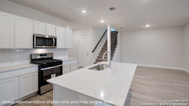 kitchen with appliances with stainless steel finishes, white cabinets, a center island with sink, and light hardwood / wood-style floors