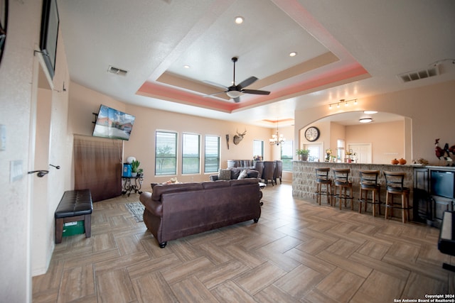 living room featuring light parquet floors, a raised ceiling, and ceiling fan with notable chandelier