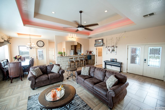 living room featuring ceiling fan with notable chandelier and a raised ceiling