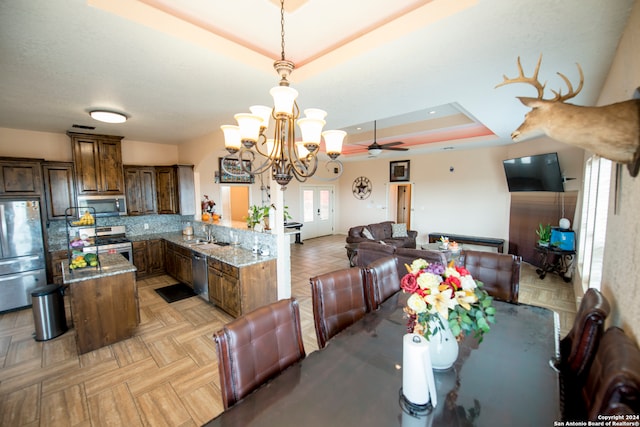 dining area featuring light parquet floors, a raised ceiling, sink, and ceiling fan with notable chandelier