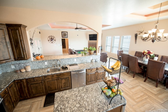 kitchen with stainless steel dishwasher, sink, light stone countertops, and a raised ceiling