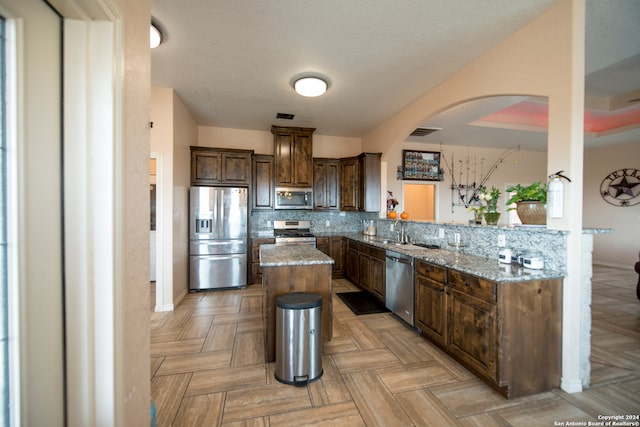 kitchen with a kitchen island, light stone countertops, kitchen peninsula, and stainless steel appliances