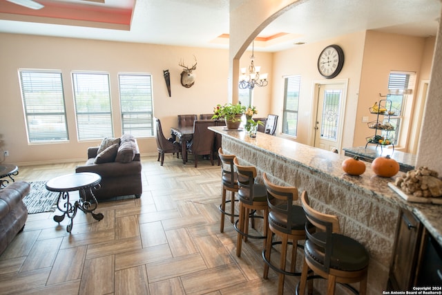 kitchen featuring a kitchen bar, parquet flooring, stone countertops, pendant lighting, and an inviting chandelier