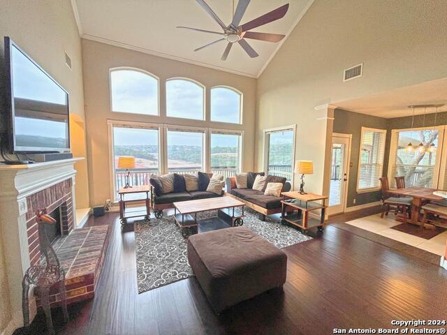 living room with a brick fireplace, dark hardwood / wood-style floors, high vaulted ceiling, and ceiling fan