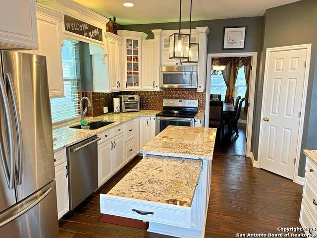 kitchen featuring appliances with stainless steel finishes, a kitchen island, hanging light fixtures, white cabinets, and dark hardwood / wood-style floors