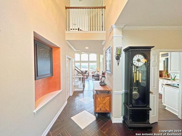 corridor with decorative columns, crown molding, dark parquet floors, and a towering ceiling