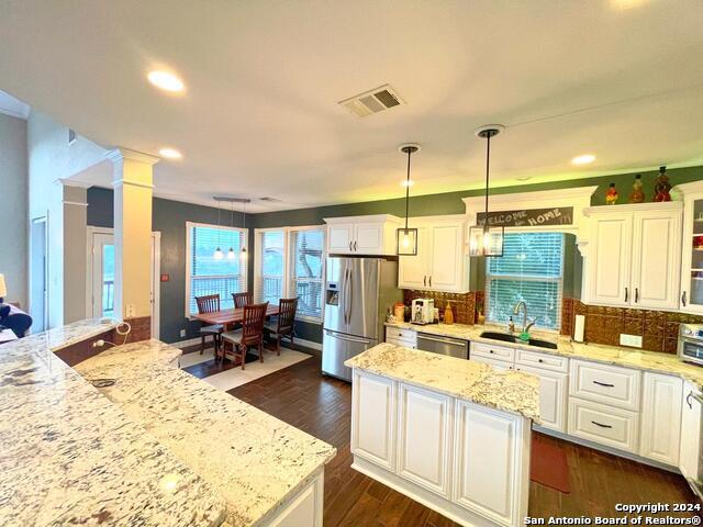 kitchen featuring decorative backsplash, white cabinetry, stainless steel appliances, decorative light fixtures, and a center island