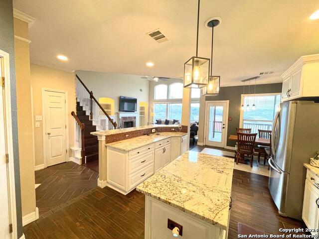 kitchen with a healthy amount of sunlight, a kitchen island, stainless steel fridge, white cabinetry, and decorative light fixtures