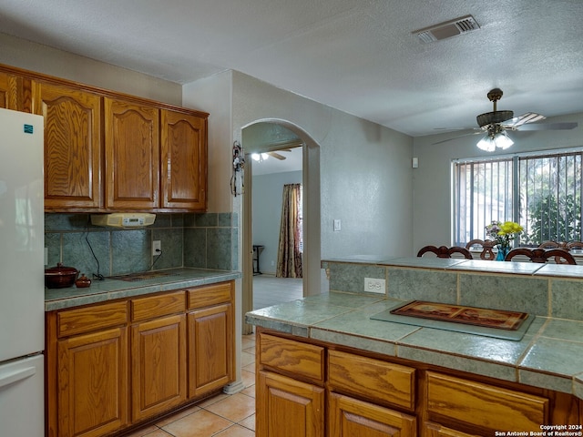 kitchen featuring white fridge, a textured ceiling, light tile patterned flooring, and tile counters