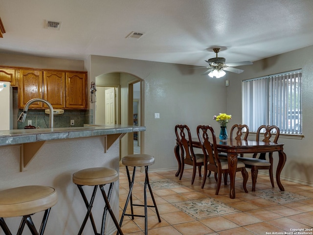 kitchen with a breakfast bar area, sink, tasteful backsplash, light tile patterned floors, and ceiling fan