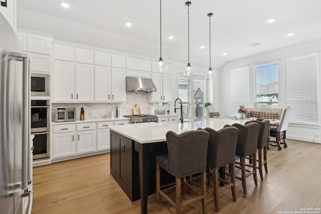 kitchen featuring extractor fan, decorative light fixtures, an island with sink, and a wealth of natural light