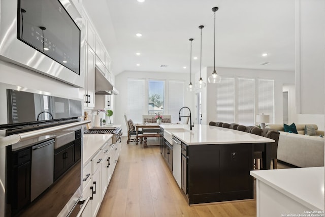 kitchen featuring sink, hanging light fixtures, white cabinetry, light hardwood / wood-style flooring, and a center island with sink