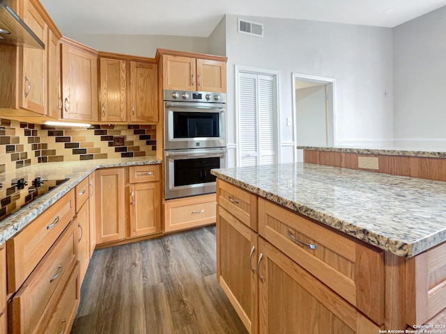 kitchen with light stone counters, stainless steel double oven, black electric stovetop, and dark wood-type flooring