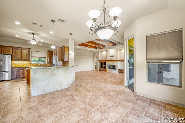 kitchen with kitchen peninsula, a tile fireplace, stainless steel fridge, pendant lighting, and ceiling fan with notable chandelier