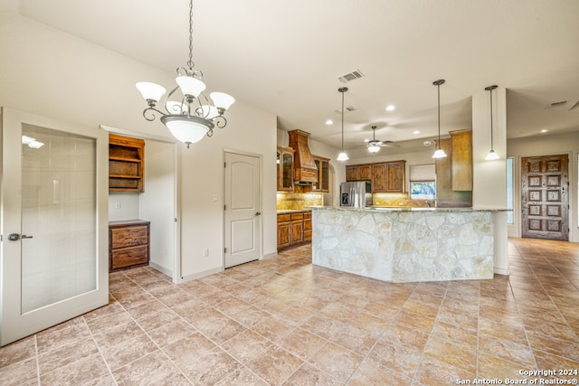 kitchen with custom exhaust hood, kitchen peninsula, backsplash, stainless steel fridge with ice dispenser, and ceiling fan with notable chandelier