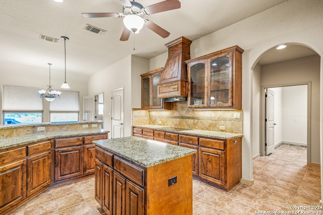 kitchen with a kitchen island, black electric stovetop, decorative light fixtures, light stone counters, and ceiling fan with notable chandelier