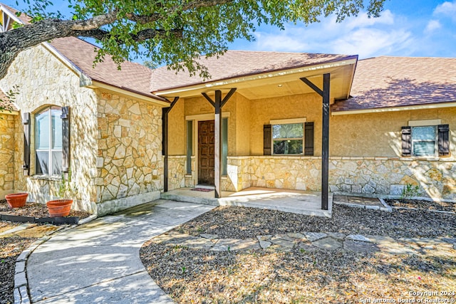 view of front facade featuring a shingled roof, stone siding, and stucco siding