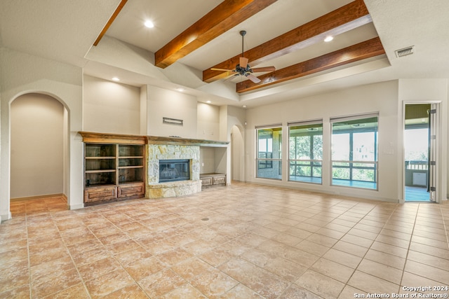 unfurnished living room with arched walkways, beam ceiling, visible vents, ceiling fan, and a stone fireplace