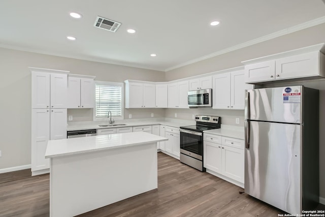 kitchen featuring appliances with stainless steel finishes, a sink, crown molding, white cabinets, and a kitchen island