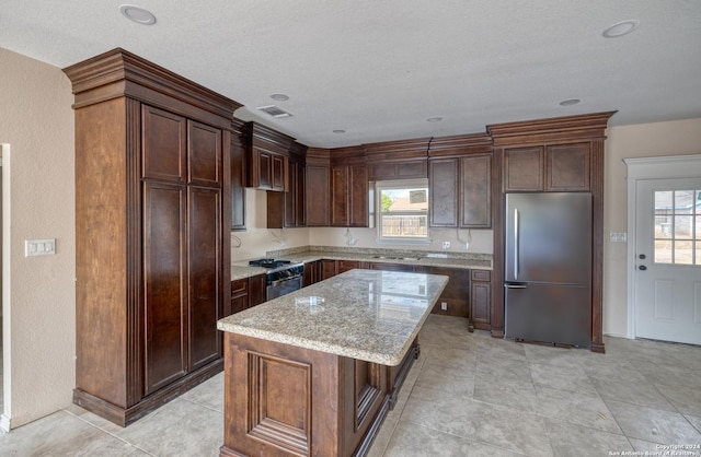 144 W Brazos St, Uvalde, TX 78801 - kitchen featuring visible vents, range with gas stovetop, a kitchen island, stainless steel fridge, and light stone counters